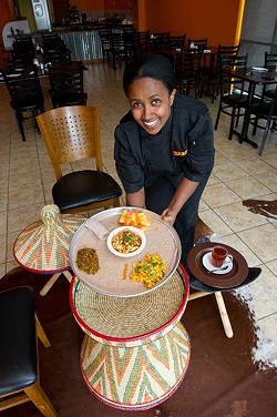 Haiget A Yosef brings Ethiopian and Kenyan cuisine Chicken Tibs with three sides, mango salad, gomen/sukamawiki, and yedenich wot to the mesob woven serving table. (Shannon Cornman)